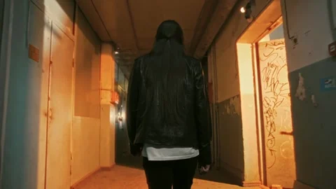 Guy in a leather jacket with long hair moves down a long narrow corridor Stock Footage 287914932