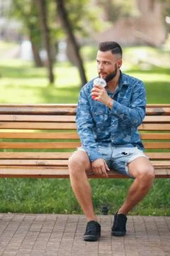 A guy with lemonade is resting in a park on a bench in the spring. Sunny day. Stock Photos