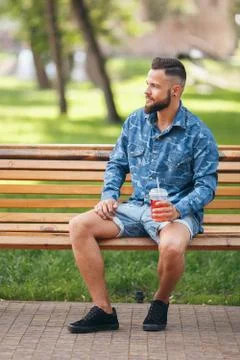A guy with lemonade is resting in a park on a bench in the spring. Sunny day. Stock Photos