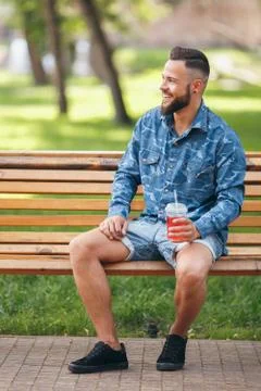 A guy with lemonade is resting in a park on a bench in the spring. Sunny day. Stock Photos