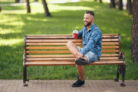 A guy with lemonade is resting in a park on a bench in the spring. Sunny day. Stock Photos