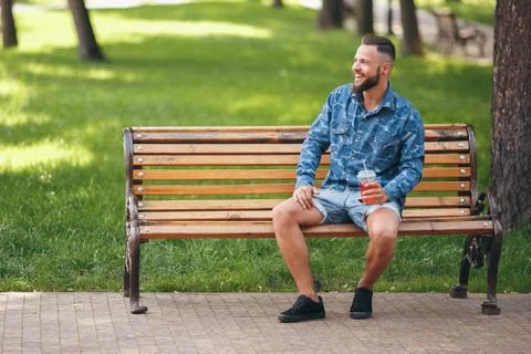 A guy with lemonade is resting in a park on a bench in the spring. Sunny day. Foto stock
