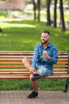 A guy with lemonade is resting in a park on a bench in the spring. Sunny day. Stock Photos