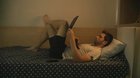 The guy lies on the bed and types on the laptop keyboard 스톡 동영상 140051325