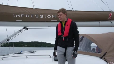 Guy with life jacket gives instruction to team on yacht deck Stock Footage 168361582