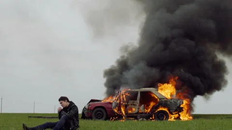 A guy lights a cigarette against the backdrop of his burning car, the harm of Stock Footage 95197990