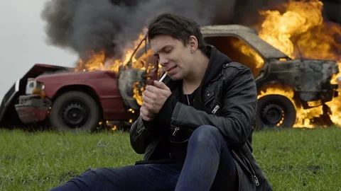 A guy lights a cigarette against the backdrop of his burning car, the harm of Stock Footage 95200416
