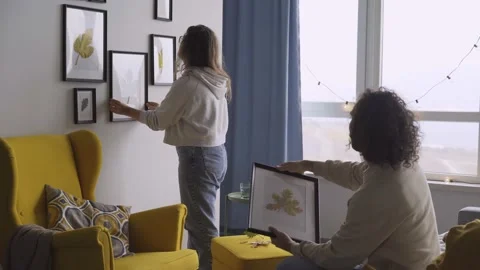Guy with long curly hair helps young woman hang frames Stock Footage 147243136