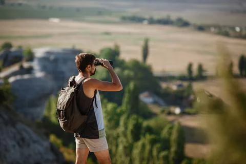 Guy looking at binoculars in hill. man in t-shirt with backpack. Stock Photos