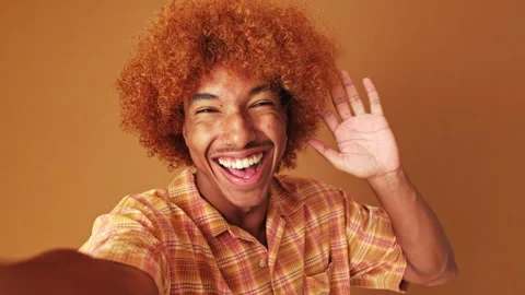 Guy looking at the camera taking selfie, victory sign, isolated on brown Stock Footage 253932876