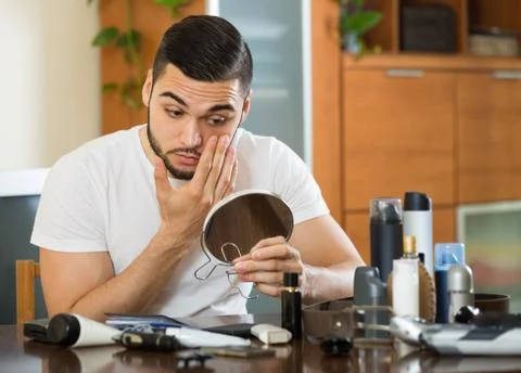 Guy looking at his problematic skin in a mirror Foto stock