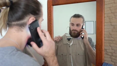 Guy is looking into the mirror Putting together an outfit Talking on smartphone Stock Footage 147894900