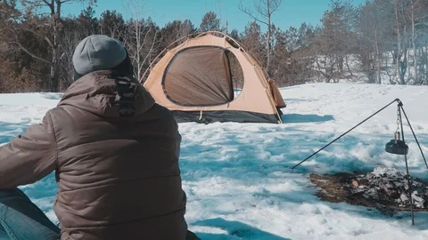 The guy is looking near the fire and tents in the winter forest Stock Footage 87586315