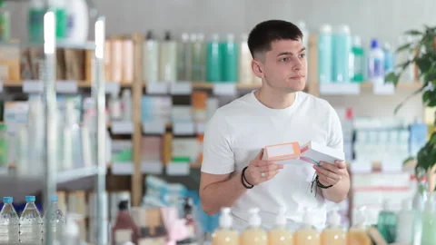 Guy is looking at the packages of medicines in the pharmacy with interest. Buyer Stock Footage 332636319