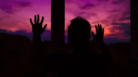 A guy looks at a beautiful sunset from the window of his apartment. Stock Photos