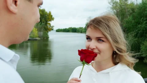 A guy in love gave a girl a red rose, and she looks at him lovingly. Stock Footage 317170053