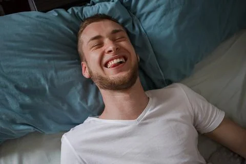 A guy lying in bed and showing his tongue Stock Photos