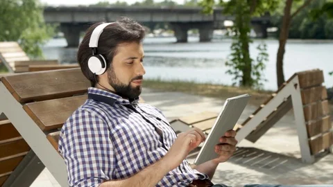 Guy is lying on bench and listening to music through headphones. Also he is Stock-Footage 99740049