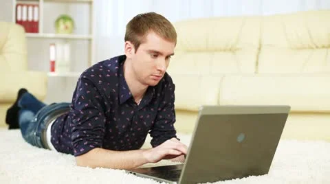 Guy lying on carpet with laptop and looking at camera. DOLLY HD Video stock 8954517