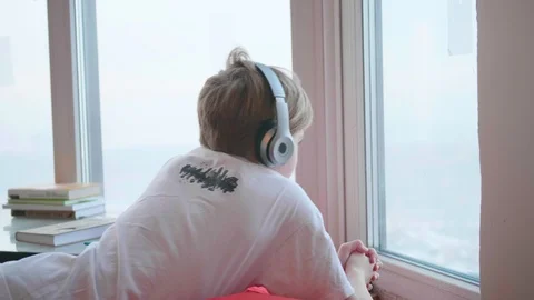 The guy is lying near the window and listening to music through headphones. The 動画素材 85696053