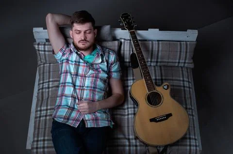 The guy is lying on the sofa with his guitar at night, top view, musician's d Stock Photos