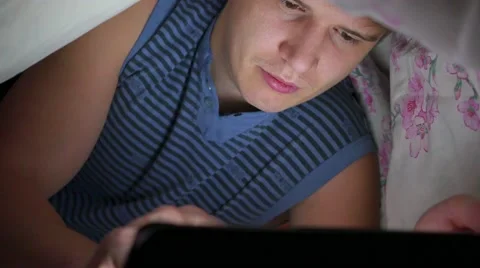 Guy lying under blanket and watching cinema on touch pad Vídeo Stock 68368529