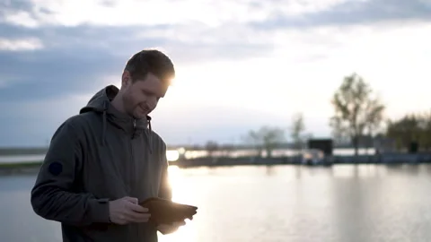 Guy is mailing using tablet or touchscreen. Tourist on the lake and sun lights. Video stock 99432630