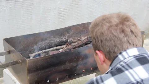 The guy makes a fire in the grill. Guy fanning the flame Stock Footage 146276384