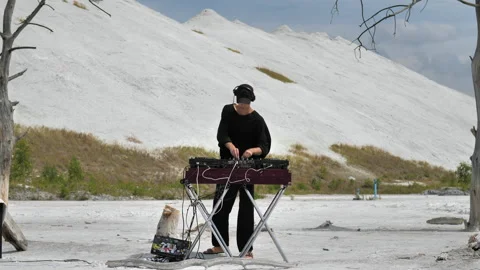 A guy making music at a DJ console in the middle of mountains of chemical waste Stock Footage 172296221
