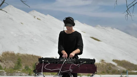 A guy making music at a DJ set in the middle of mountains of chemical waste Stock Footage 172314748