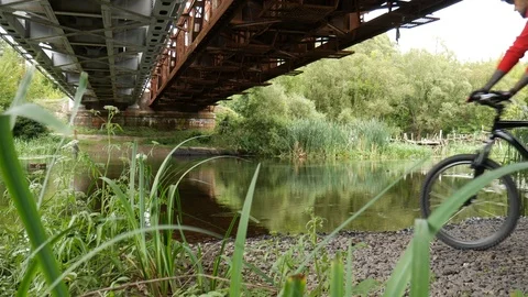 Guy man with a bike sitting under a bridge by the river Stock Footage 113727741
