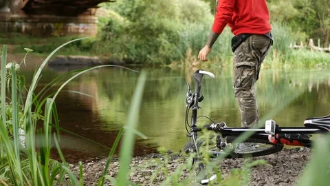 Guy man with a bike sitting under a bridge by the river Stock Footage 113727752