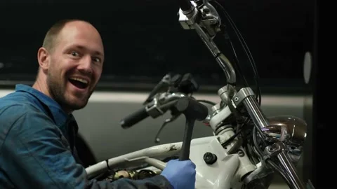 Guy mechanic in blue overalls next to a motorcycle Stock Footage 162391451
