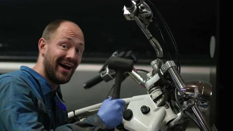 Guy mechanic in blue overalls next to a motorcycle Stock Footage 162391686