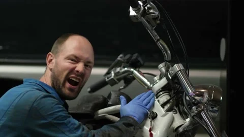 Guy mechanic in blue overalls next to a motorcycle Stock Footage 162391869
