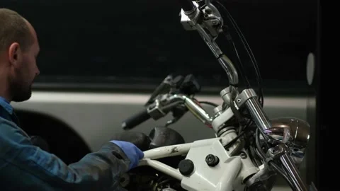 Guy mechanic in blue overalls next to a motorcycle Stock Footage 162392371