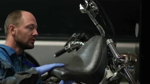 Guy mechanic in blue overalls next to a motorcycle Stock Footage 162393557