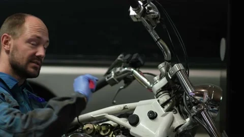 Guy mechanic in blue overalls next to a motorcycle Stock Footage 162393880