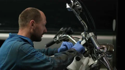 Guy mechanic in blue overalls next to a motorcycle Stock Footage 162394856