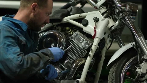 Guy mechanic in blue overalls next to a motorcycle Stock Footage 162395286