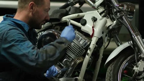 Guy mechanic in blue overalls next to a motorcycle Stock Footage 162395853