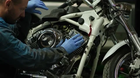 Guy mechanic in blue overalls next to a motorcycle Stock Footage 162396562