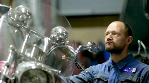 Guy mechanic in blue overalls next to a motorcycle Stock Footage 162398681
