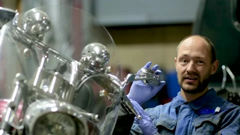 Guy mechanic in blue overalls next to a motorcycle Stock Footage 162399126