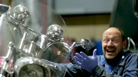 Guy mechanic in blue overalls next to a motorcycle Stock Footage 162399425