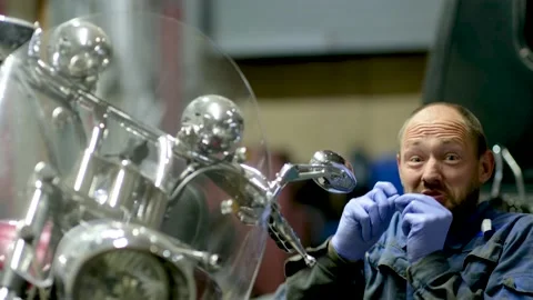 Guy mechanic in blue overalls next to a motorcycle Stock Footage 162399691