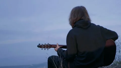 A guy in the mountains is hiking and playing the guitar Stock Footage 254933364