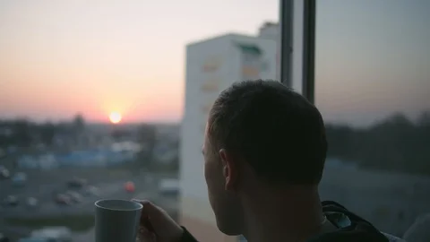 A guy with a mug of tea stands on the balcony during sunset Stock Footage 129040071