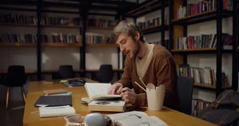 A guy with a mustache and beard sits at a table opens books and takes notes Stock Footage 313356999