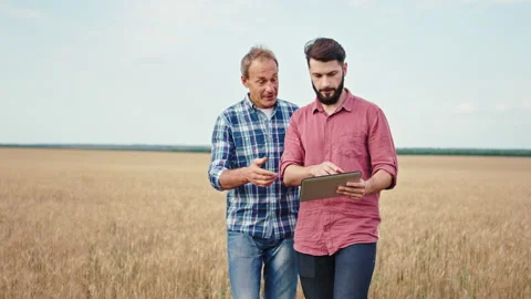 Guy with a new gadget electronic tablet and his father farmer walking through Stock Footage 136309102